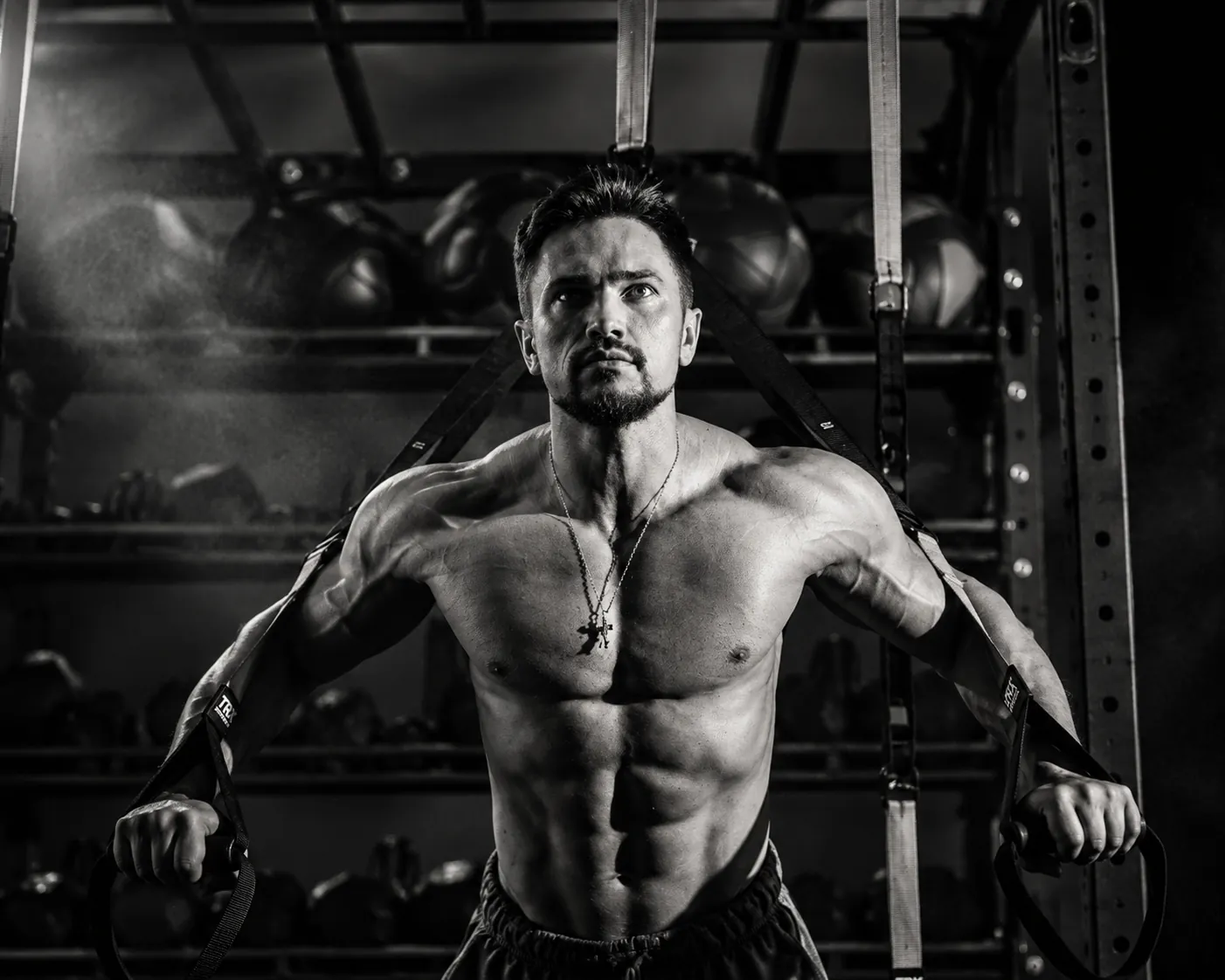 Black-and-white photo of Coach Artem Piari posing in front of a squat rack